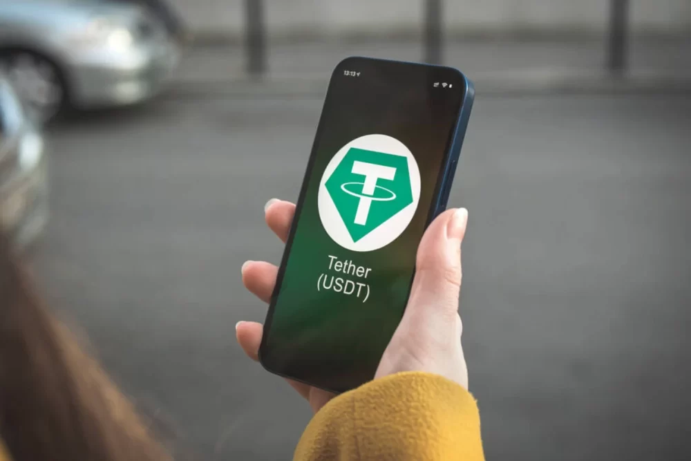 Someone holding a smartphone with the Tether logo displayed on screen.