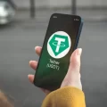 Someone holding a smartphone with the Tether logo displayed on screen.
