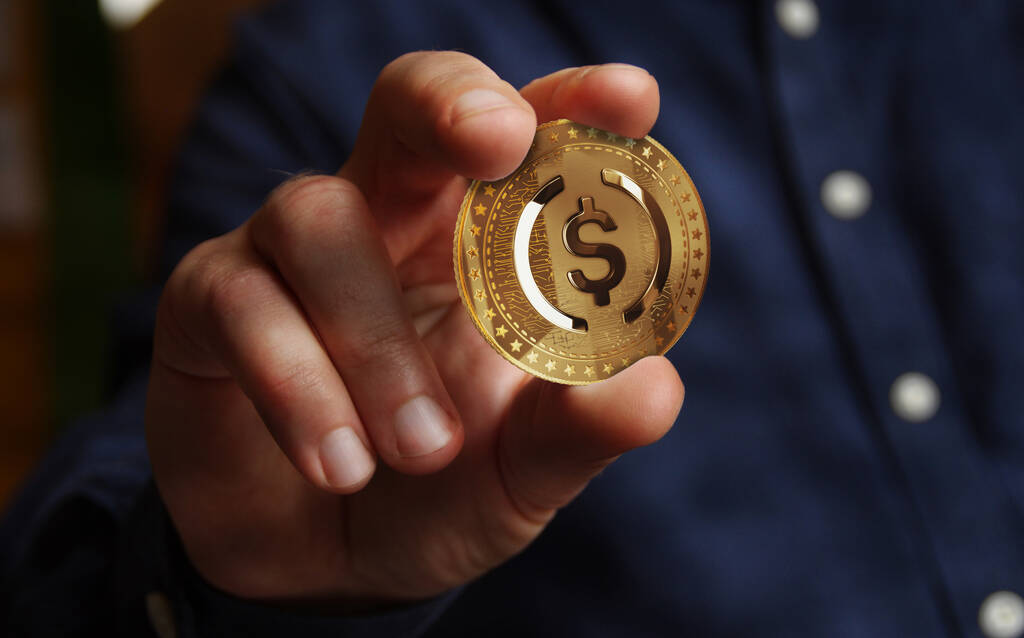 A man holding up a USD coin against the screen.